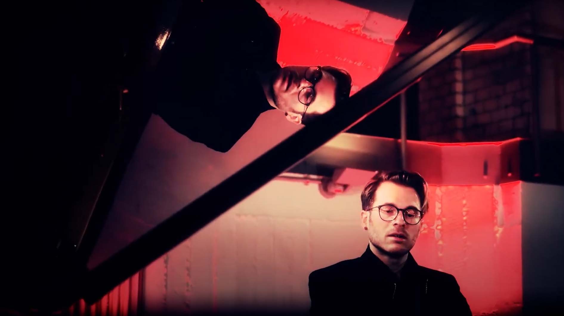Ein Mann mit Brille spielt Klavier, spiegelt sich im Flügeldeckel. Rotes Licht im Hintergrund.